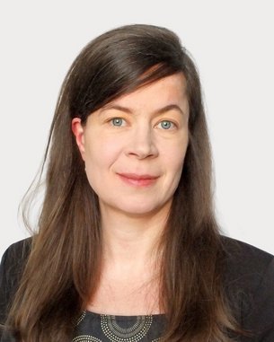 Eine Frau mit langen, braunen Haaren und blauen Augen trägt ein schwarzes Oberteil mit einem grafischen Muster.