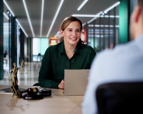 Rechtspsychologie - SRH Fernhochschule Eine Frau in einem grünen Hemd sitzt an einem Tisch und spricht mit einem Mann. Auf dem Tisch steht eine Statue der Justitia.
