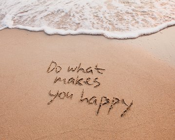 Im Sand geschriebenen Text: „Do what makes you happy“, mit Wellen, die sanft den Strand berühren.