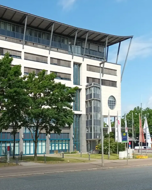 Moderne Bürogebäude mit Glasfront und markanter Dachkonstruktion, umgeben von Bäumen und Fahnen.