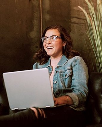 Abendstudium Psychologie Eine Person mit Brille sitzt auf einer Ledercouch und arbeitet an einem Laptop. Im Hintergrund ist eine Pflanze sichtbar.